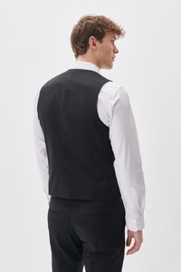 Schwarze formelle Weste mit glatter Oberfläche, die eine taillierte Passform und einen hohen Rücken hat. Getragen über einem weißen Hemd mit knöpfbaren Manschetten.