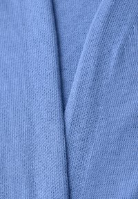 Tissu tricoté bleu clair doux avec un détail de couture chevauchante visible en gros plan.