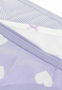 Lila Baumwollstoff mit weißen Herzenmuster, ergänzt durch ein helllila gestreiftes Design, das mit einer dekorativen Schleifenakzent versehen ist.