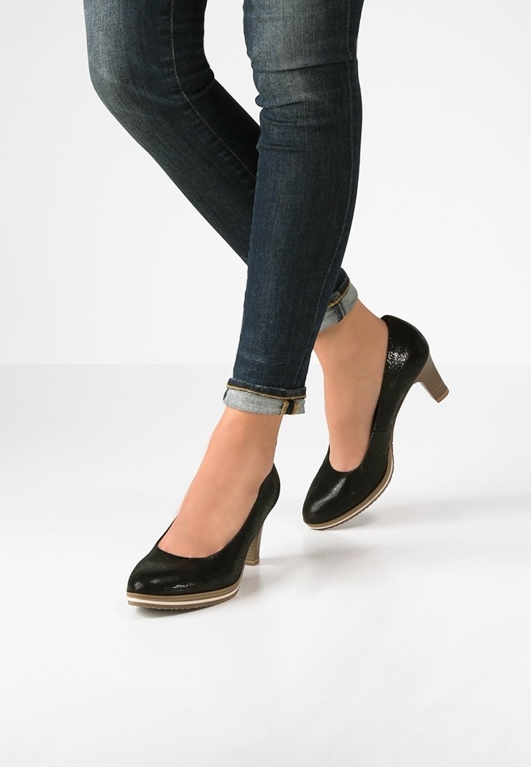 Svarta lackläderklackar med rund tå, låg klack och en ljusfärgad plattformdetalj, bärs med mörkblå uppvikta jeans.