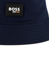 Marine blauwe emmerhoed van duurzame stof met een gestikte rand, een rechthoekige zwarte patch met het "BOSS" logo in witte en oranje accenten.