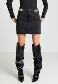 Schwarzer Jeans-Minirock mit ausgefranstem Saum und verzierendem Bund; kombiniert mit glänzenden schwarzen kniehohen Stiefeln mit spitzen Zehen.