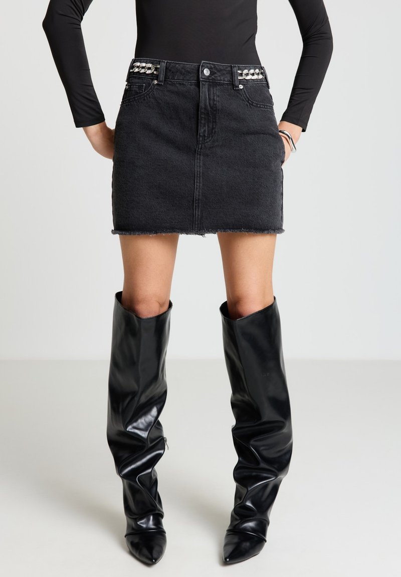 Schwarzer Jeans-Minirock mit ausgefranstem Saum und verzierendem Bund; kombiniert mit glänzenden schwarzen kniehohen Stiefeln mit spitzen Zehen.