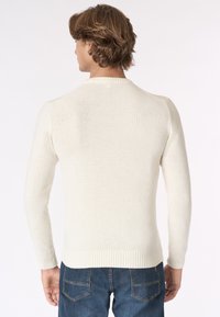 Maglione a maglia color crema con maniche lunghe e scollatura rotonda. Orlo e polsini a coste, tessuto texturizzato. Indossato con jeans blu.