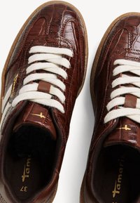 Paire de baskets en cuir marron avec un motif crocodile, lacets blancs, semelles en gomme et logo de la marque doré sur la languette et le côté.