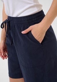 Marineblaue Shorts aus weichem Material, mit elastischem Bund und Kordelzug, seitlichen Taschen und lockerer Passform.