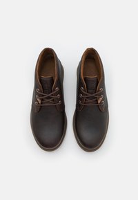 Zapatos de cuero marrón con puntas redondeadas, cordones marrones en contraste y una textura suave. Detalle de costura notable a lo largo del borde superior.