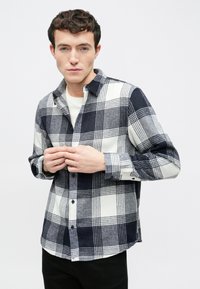 Męska koszula w kratę w kolorze granatowym i białym, wykonana z teksturowanego materiału, z zapięciem na guziki, kołnierzem w szpic i długimi rękawami.