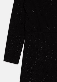 Jumpsuit nero con maniche lunghe, caratterizzato da una superficie testurizzata e macchioline argentate sparse per un effetto scintillante. Design semplice con cucitura in vita.