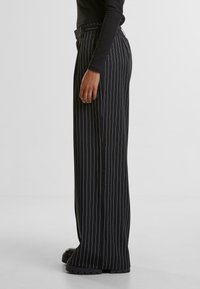 Pantaloni negri cu dungi verticale, cu talie înaltă și un design cu picior larg, având o croială ajustată, cusături vizibile și pantofi cu platformă groasă, negri.