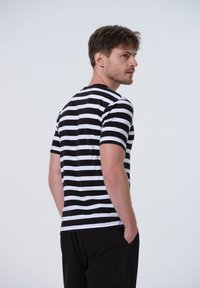 Sort og hvid stribet t-shirt med korte ærmer og rund hals, der har en afslappet pasform og blød tekstur. Bæres med sorte bukser.