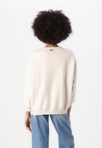 Cremfarbener Sweatshirt mit strukturierter Stoffqualität und lockerer Passform, mit einem gerippten Halsausschnitt und Saum sowie einem kleinen Etikett auf der Rückseite.