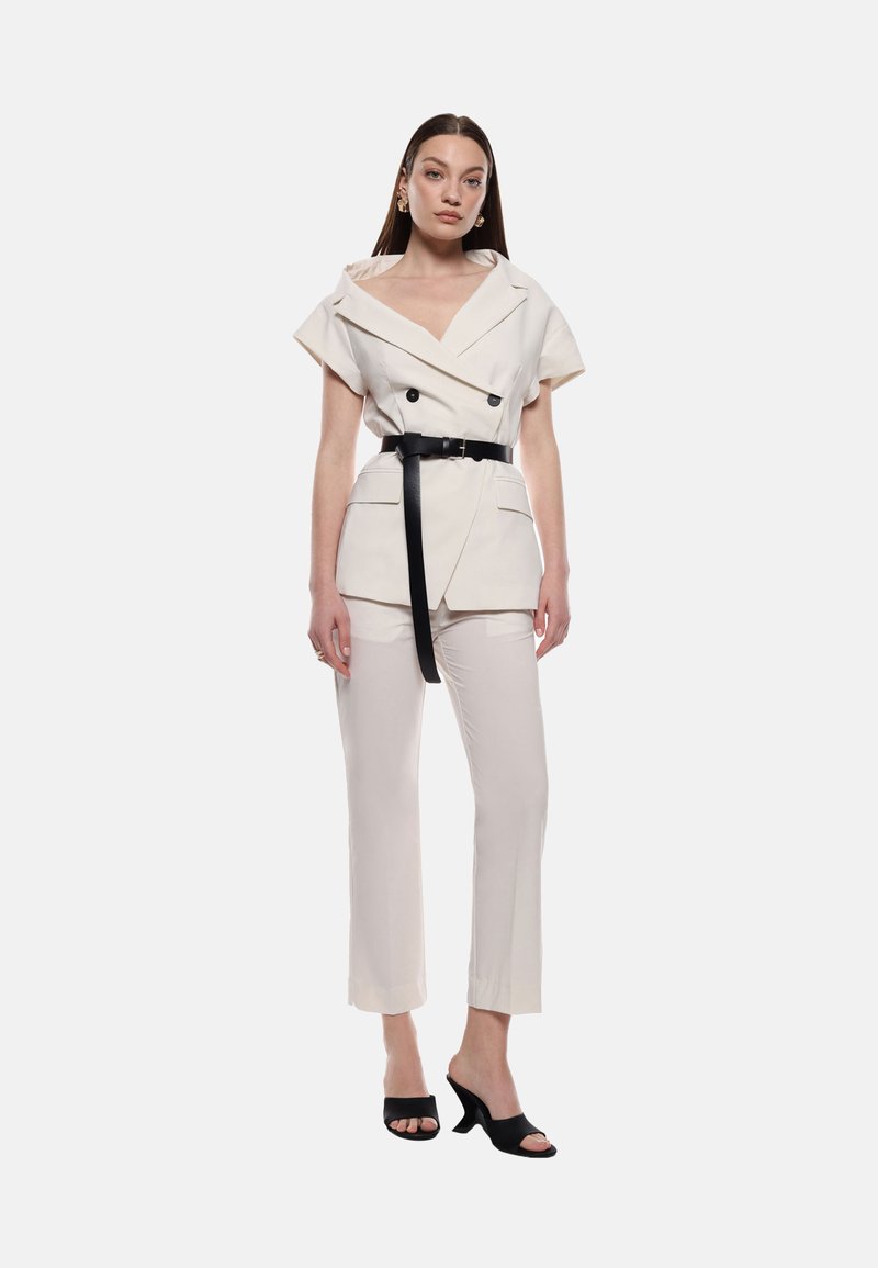 Completo su misura color crema con maniche corte, design doppiopetto, cintura nera e pantaloni svasati. Le mule nere con tacco completano il look.