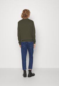 Sudadera verde oliva con cuello redondo, puños acanalados, combinada con jeans de mezclilla azul y botas negras hasta el tobillo. Corte simple y relajado.