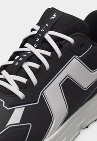 Αθλητικό παπούτσι ασπρόμαυρο με λευκά κορδόνια, τολμηρά γεωμετρικά σχέδια και τη λέξη "THUNDER" τυπωμένη στην ταμπέλα της γλώσσας.