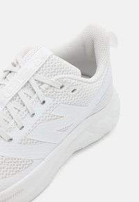 Chaussure de sport blanche en tissu en maille avec une surface texturée, dotée de lacets, d'un col rembourré et d'une semelle épaisse et amortissante.