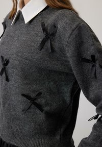 Grijze gebreide trui met zwarte lintaccenten op de schouders, met een ronde halslijn en lange mouwen. Getextureerde stof met geribbelde zoom.
