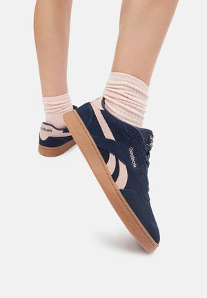 Niebieskie zamszowe sneakersy typu high-top z różowymi akcentami, charakteryzujące się teksturowaną powierzchnią i gumową podeszwą, wyeksponowane z zwiniętymi różowymi skarpetkami.
