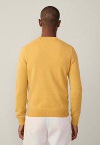 Žlutý pletený svetr s kulatým výstřihem, žebrovanými manžetami a spodním lemem a měkkou texturou, zobrazený zezadu na neutrálním pozadí.