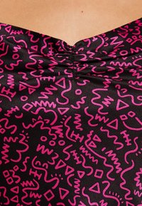 Svart tyg med ett färgglatt abstrakt mönster i klar rosa som har snirkliga linjer och geometriska former vid halsområdet.