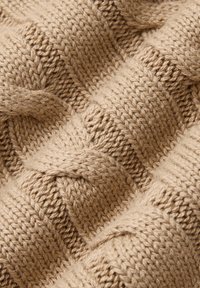 Dzianina w jasnobeżowym kolorze z teksturowanym, warkoczowym wzorem. Tkany materiał ma naprzemiennie gładkie i żeberkowane części, co nadaje mu głębię.