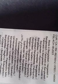 Etykieta z wieloma liniami tekstu w różnych językach, wskazująca "Wyprodukowano w Bangladeszu." Materiał wydaje się biały z czarnym nadrukiem.