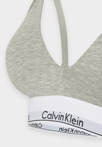 Svijetlosivi bralet s mekom teksturom, s v-izrezom i tankim naramenicama. Bijela traka s natpisom "Calvin Klein" ispisanim crnom bojom.