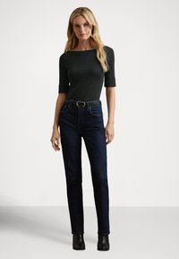 Στενή μπλούζα σκούρου πράσινου χρώματος με μανίκια τριών τετάρτων, συνδυασμένη με ψηλόμεσα μπλε τζιν και μαύρα μποτάκια αστραγάλου. Απλός σχεδιασμός, χωρίς σχέδια.