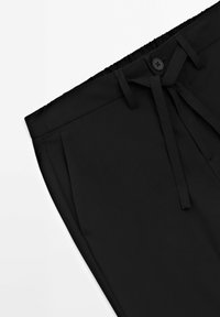Schwarze Hosen mit glatter Textur, elastischem Bund, Knopfverschluss und Kordelzug. Sie verfügen über Seitentaschen und einen taillierten Schnitt.