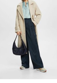 Beige ullkappa, ljusblå blus, marinblå vida byxor, svart axelremsväska och sportiga sneakers i dämpade toner med en texturerad design.