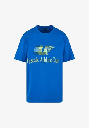 Sinine puuvillane T-särk, millel on graafiline disain ja kollane tekst "Upscale Athletic Club" ning stiliseeritud "U" logo.