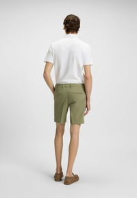 Pantalones cortos de algodón en verde oliva con un corte recto, que cuentan con bolsillos traseros y una cinturilla. Combinados con un polo de manga corta blanca y lisa.