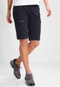 Černé kraťasy do kolen vyrobené z lehkého, pružného materiálu s kapsami na zip. Na sobě má šedé a růžové outdoorové boty.