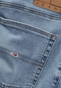 Gesäßtasche einer blauen Jeans mit brauner Naht, kleinem rot-weiß-blauem Flaggenlogo und einem Lederpatch mit dem Schriftzug "JEANS."