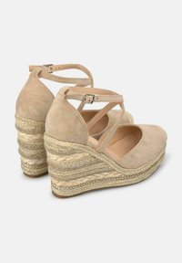 Sandali con zeppa in suede beige, caratterizzati da cinturini incrociati e una piattaforma in juta decorata. Presentano un design intrecciato e un sistema di chiusura con fibbia.