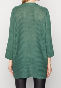 Grön stickad oversized tröja med en lös passform, sänkta axlar och trekvartsärmar. Texturerat mönster genom hela plagget.