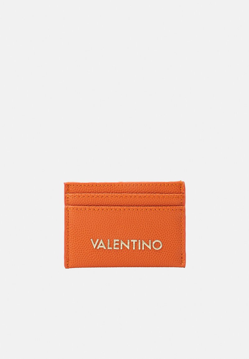 Oranžs ādas kredītkaršu turētājs ar zelta "VALENTINO" logo, četriem karšu nodalījumiem un teksturētu virsmu labākai satveršanai. Kompakta taisnstūrveida forma.