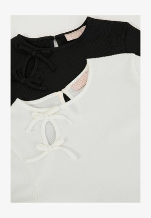 Fekete-fehér topp, bordázott textúrával, rövid ujjakkal, kerek nyakkivágással és díszes masnikkal az elülső nyitásnál.