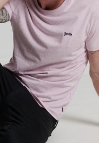 Roze katoenen t-shirt met korte mouwen, ronde hals en klein zwart logo op de borst. Zachte textuur, ontspannen pasvorm.