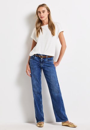 Weißes kurzärmliges Oberteil aus strukturiertem Stoff, Jeans in weitem Schnitt in Blau mit Gürtel und goldene Ballerinas mit Schleifendetail. Einfaches und lässiges Outfit.