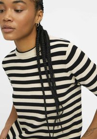 Schwarz-weißer, gestreifter Kurzarm-Strickpullover mit Rundhalsausschnitt und geripptem Saum. Das Model hat lange geflochtene Haare und trägt Creolen.