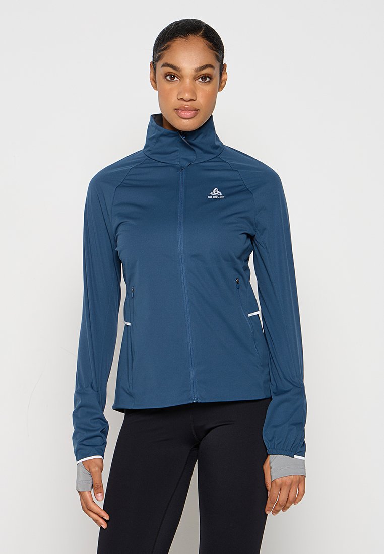 Dunkelblaue Sportjacke, mit Reißverschluss vorne, hohem Kragen, zwei Seitentaschen, reflektierenden Akzenten, dehnbarem Stoff und Daumenlöchern in den Ärmeln.