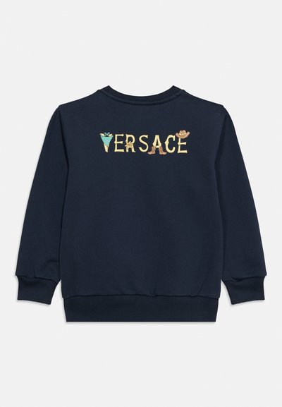 Μπλε σκούρα φούτερ με το κείμενο "VERSACE" στην πλάτη, κάθε γράμμα διακοσμημένο με στοιχεία σε western θέμα όπως καπέλο καουμπόη και μπότες.
