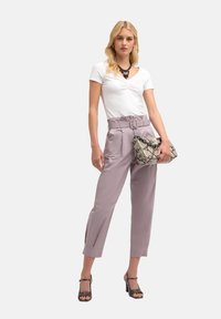 Biała koszulka z krótkim rękawem z gromadzonym przodem, zestawiona z jasnofioletowymi spodniami z wysokim stanem i paskiem. Trzyma wzorzysty kopertówkę i nosi sandały na obcasie.