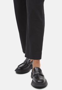 Person wearing black wide-leg pants and black chunky platform loafers standing on a white background.