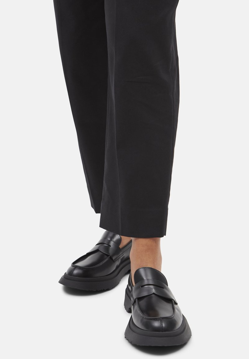 Person wearing black wide-leg pants and black chunky platform loafers standing on a white background.