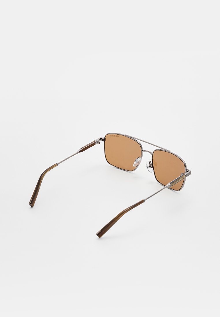 Sonnenbrille mit einem silbernen Metallrahmen, braun getönten Gläsern und strukturierten braunen Bügeln. Winkelige Form mit einem minimalistischen Design.