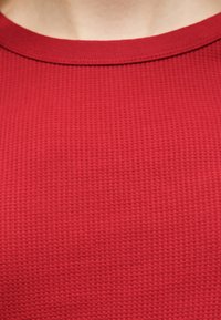 Κοντινό πλάνο κόκκινου υφάσματος με υφή και στρογγυλή λαιμόκοψη στο άνω μέρος του στήθους και το λαιμό ενός ατόμου.