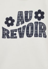 Bijela majica s mornarsko plavim grafičkim natpisom "AU REVOIR" i dva cvjetna akcenta. Natpis ima teksturirani uzorak.
