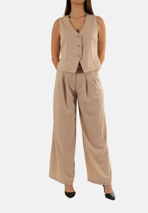 Gilet beige ajusté à trois boutons, assorti à un pantalon large de la même couleur. Tissu lisse et léger ; talons noirs.